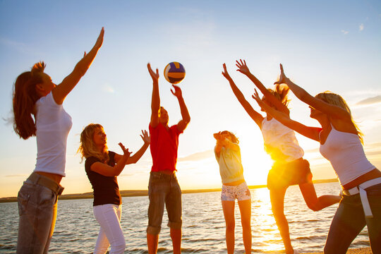 group of young men and women play beach volleyball together on the coast on a summer day