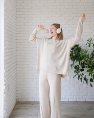 young millennial woman listening to the music at home standing next to the window dancing