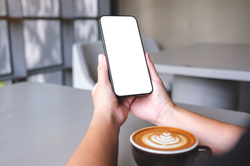 Mockup image of a woman holding and using mobile phone with blank desktop screen in cafe