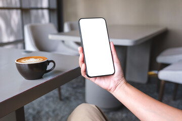 Mockup image of a woman holding and using mobile phone with blank desktop screen in cafe