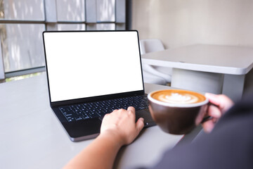 Mockup image of a woman working on laptop computer with blank white desktop screen while drinking coffee in cafe