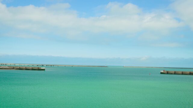 View of open sea while exiting Dunkirk port on clear sunny day. Turquoise water stretching between harbor walls under blue sky. Calm ocean horizon appearing at gateway from French coastal harbor