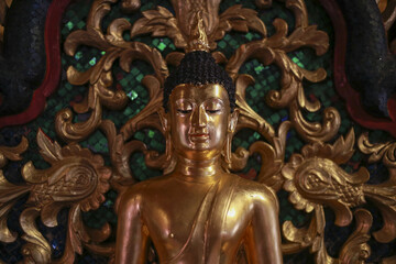Golden buddha statue radiates serene and peaceful aura, symbolizing meditation and spiritual enlightenment. Ornate carving creates an intricate background for this ancient religion found temple