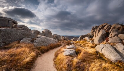 Dirt Path Winding Through Rocky Cliffs With Gray Boulders And Golden Grass Under A Cloudy Sky Creates An Adventurous Exploration Scene