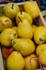 A vibrant display of fresh yellow pears arranged in a rustic wooden basket at a busy farmers market