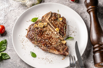 T-bone steak with garlic and herbs on plate with cutlery
