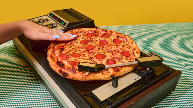 Closeup of hand pressing pizza onto spinning vinyl turntable in retro concept. Idea of psychology and emotions, social media and digital content, retro technology, design and creative expression. - Powered by Adobe