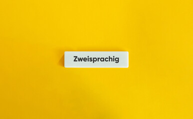 Zweisprachig Text auf weißem Buchstaben-Kachel vor gelbem Hintergrund