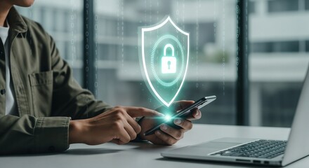 A person in a green jacket sits at a desk with a laptop and uses a smartphone. A large, glowing holographic security shield with a padlock icon floats above the phone. Digital rain of binary code fall
