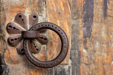 Close-up of old rusty metal hanging ring door knob covered with geometric ornament on wooden door