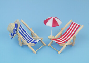 Blue and red beach chairs with hat and umbrella on blue background. Copy space for text. Travel and vacation concept.