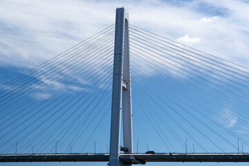 A detailed view of the Meiko Chuo Bridge, a white cable-stayed bridge in Nagoya Port, Japan. The geometric lines of the cables create a modern and dynamic composition under a clear blue sky.