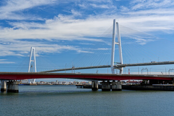 The Meiko Chuo Bridge and the red Kinjyo Bridge spanning Nagoya Port, Japan. A white cable-stayed bridge and a red girder bridge create a striking contrast under a bright blue sky.