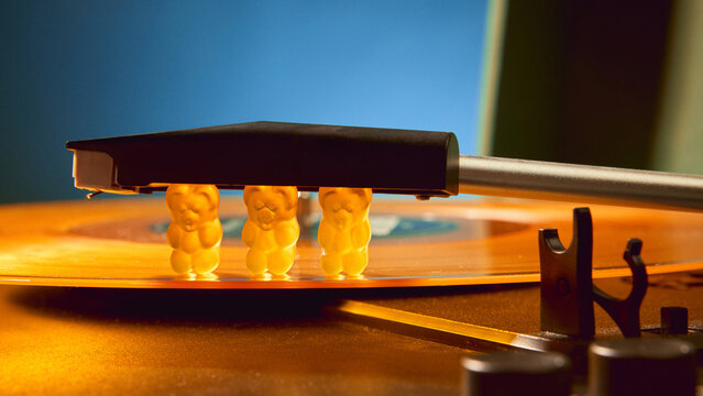 Gummy bears pressed under needle of retro vinyl record player with surreal emotion. Concept of music and audio, creative surrealism, cultural imagination, and symbolic lifestyle design.