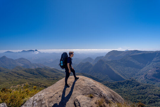 A hiker with a backpack on the mountaintop along the long-distance trail between the cities of Petr&oacute;polis and Teres&oacute;polis, in the mountainous region of Rio de Janeiro, enjoying a beautiful panoramic v