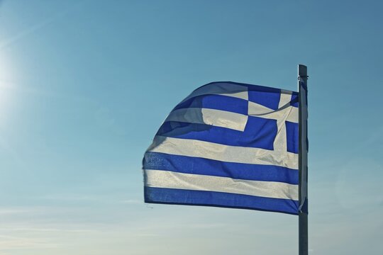 The Greek flag flies in the wind against a clear blue sky with sunshine, Church of the Virgin Mary Tsambika (Kyra Psili), Archangelos, Rhodes Island, Greece