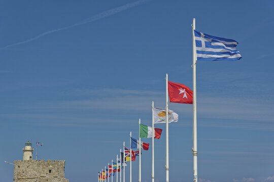 Several flags waving in the wind against a clear blue sky, including the Greek flag, Mandraki Harbour, Medieval Town of Rhodes, Rhodes Island, Greece