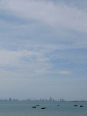 calm blue sea with fishing boats and distant city skyline under wide cloudy sky