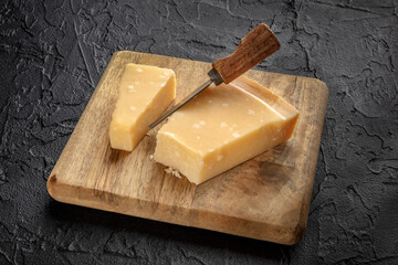 Parmesan cheese wedge on a wooden cutting board, with a cheese knife, on a black slate background