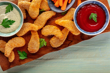 Chicken nuggets with fresh vegetables and dips, on a wooden table, overhead flat lay shot with copy space
