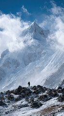 Awe inspiring view of lone hiker standing in solitude before majestic snow covered mountain peak. An extreme adventure in vast high altitude winter landscape