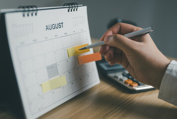 Close-up young woman organizing her schedule on calendar with sticky notes, marking important dates for business planning and time management. meeting schedule. selective focus