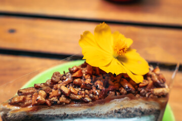 Delicious dessert slice, rich chocolate cake topped with nuts and a vibrant yellow flower, perfect for a sweet celebration.