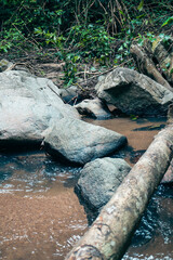 Serene natural setting, smooth rocks beside a gentle stream, lush greenery surrounds the water, perfect for relaxation or nature themes.