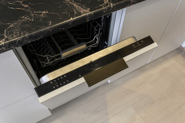 Open dishwasher with a black control panel under a dark marble countertop in a modern kitchen