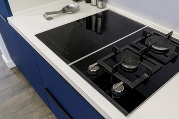 A modern kitchen featuring a combination gas and induction cooktop set in a white countertop. Blue cabinets and wood-look flooring complete the sleek design