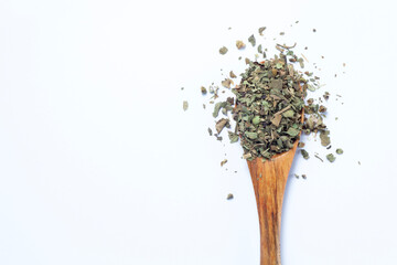 dried and chopped basil spice in a wooden spoon on white background, top view