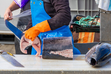 Fisherman cutting fresh tuna on table at market, close-up of fish processing, seafood preparation and traditional fishing industry scene.