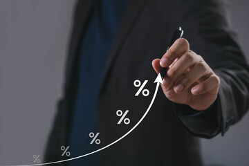 Businessman drawing rising curve with percentage signs, symbolizing financial growth, interest rate...