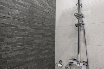 Modern bathroom detail featuring dark textured wall tiles and a chrome shower set against light,...