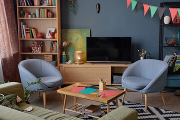 Empty living room decorated for Kwanzaa celebration with colorful paper, pencils, and festive pennant garland on wall, modern furniture arranged around wooden coffee table