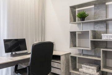 modern workspace with a desk, computer, black office chair, and gray stone-effect shelves. A plant sits on one of the shelves, adding a touch of greenery