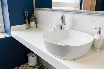 Clean bathroom featuring a round white sink, white countertop, blue wall, herringbone tile backsplash, and decorative accessories