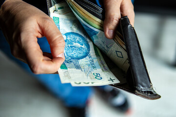 Person pulling out a 50 Polish zloty banknote from a leather wallet. Close-up shot symbolizing spending, cash payment
