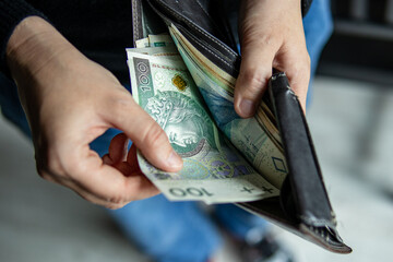 Close-up of hands pulling a 100 Polish zloty banknote from a wallet. Concept of cash transaction, finance, personal spending