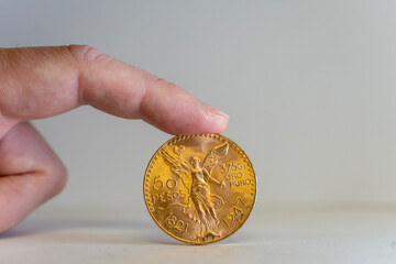 Une pièce en or 50 pesos mexicain tenu debout par un doigt