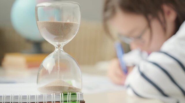 Teenager Student studying doing homework at desk with hourglass, education, knowledge and time management, writing, learning process, exam prep, child training, concentration and discipline sand timer