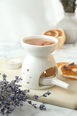 Aroma lamp with burning candle, lavender and dry orange slices on white table, closeup