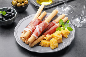 Grissini breadsticks with prosciutto, cheese and olives on grey table, closeup