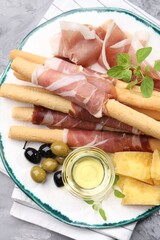 Grissini breadsticks with prosciutto, cheese, olives and honey on grey table, top view