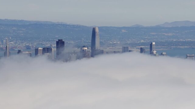 Dense clouds part to reveal San Francisco's skyline, including the Transamerica Pyramid and Salesforce Tower, in a smooth aerial ascent.