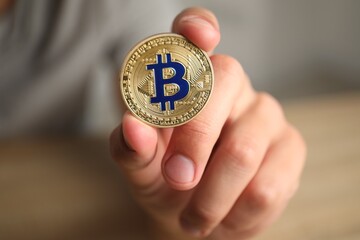 Cryptocurrency. Man holding golden bitcoin against blurred background, closeup