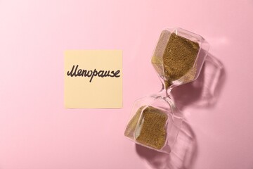 Paper note with word Menopause and hourglass on pink background, top view