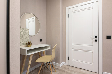 A cozy entryway featuring a white door, console table with a round mirror, and a modern chair. Neutral tones create a serene and stylish atmosphere