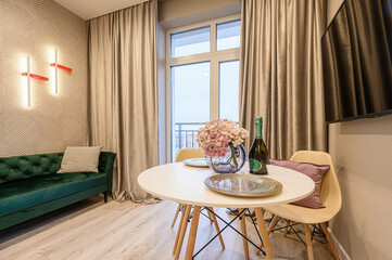 Cozy living room with a green velvet couch, round table with flowers and champagne, and a TV