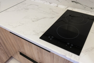 A modern kitchen counter with a white marble-patterned surface and a built-in black induction...